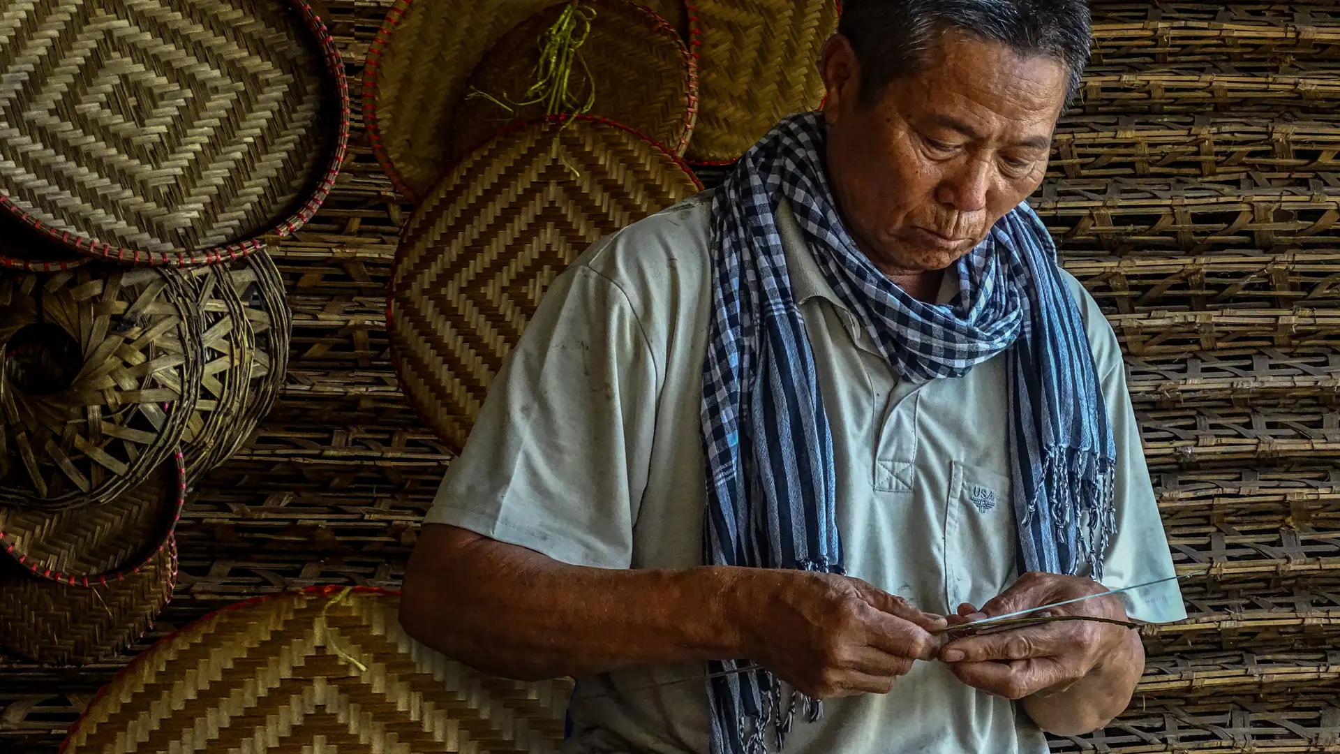 An artisan weaving a basket by hand, surrounded by finished woven panels